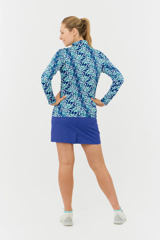 The Pure Golf Serenity long-sleeve ladies golf zip top showcases a tranquil aquatic design in varying blue and ocean hues, featuring a floating palm print. It offers a regular fit and 4-way stretch, providing comfort and a flattering shape for all body types. The mock neck collar adds a touch of elegance. Crafted from 95% Polyester and 5% Spandex, the top also boasts anti-crease, anti-static, and quick-dry features, along with UPF 50+ sun protection, making it both stylish and practical.