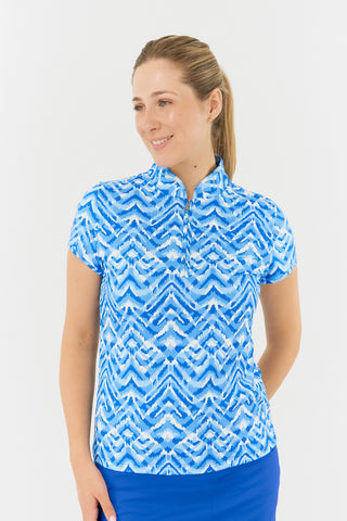 The  Pure Golf Rise Santorini Skies Cap Sleeve Ladies' Golf Polo Shirt showcases a captivating Ikat-inspired design in shades of blue and white close-up front model shot. A regular fit and 4-way stretch, it offers a flattering shape for all body types. The mandarin collar adds an elegant touch. Made from 95% polyester and 5% spandex, it provides anti-crease, anti-static, and quick-dry properties, along with UPF 50+ sun protection. Paired with a Royal Blue Skort, it completes a stylish look. 