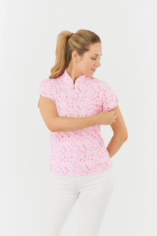 The Pure Golf Rise cap sleeve ladies' golf polo shirt in Soft Sakura, shown in a front model shot, features a subtle print of lilac, pink, and white petals set against a light pink backdrop. Designed with a regular fit, it offers 4-way stretch for a flattering shape on all body types. The mandarin collar adds a touch of elegance. Made from 95% Polyester and 5% Spandex, the shirt provides anti-crease, anti-static, and quick-dry properties, along with UPF 50+ sun protection. 