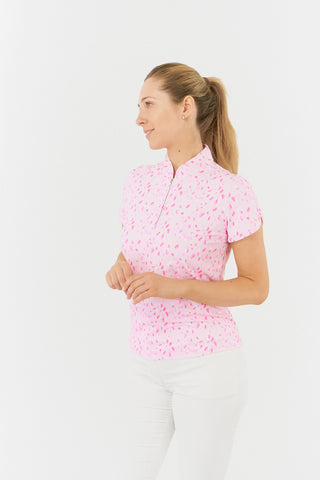 The Pure Golf Rise cap sleeve ladies' golf polo shirt in Soft Sakura, shown in a side model shot, features a subtle print of lilac, pink, and white petals against a light pink backdrop. Designed with a regular fit, it offers 4-way stretch for a flattering shape on all body types. The mandarin collar adds elegance. Made from 95% Polyester and 5% Spandex, the shirt provides anti-crease, anti-static, and quick-dry properties, along with UPF 50+ sun protection. 