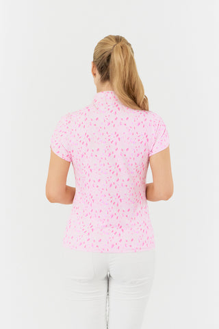 The Pure Golf Rise cap sleeve ladies' golf polo shirt in Soft Sakura, in a side model shot, showcases a subtle print of lilac, pink, and white petals against a light pink backdrop. Designed with a regular fit, it provides 4-way stretch for a flattering shape on all body types. The mandarin collar adds a touch of elegance. Made from 95% Polyester and 5% Spandex, the shirt offers anti-crease, anti-static, and quick-dry properties, along with UPF 50+ sun protection.