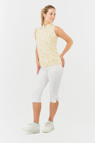 The Pure Golf model shot of the Rise Sleeveless ladies' polo shirt boasting a striking Sun Kissed print with warm honey tones. Designed with a regular fit, it offers a 4-way stretch for comfort and a flattering shape on all body types. The stylish Mandarin collar adds a fashionable touch. This polo is made from 95% Polyester and 5% Spandex, offering anti-crease, anti-static, and quick-dry properties, along with UPF 50+ sun protection. Paired With White Trust Capri's.  