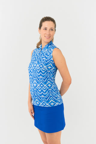 The side view of the Pure Golf Rise Santorini Skies Sleeveless Ladies' Golf Polo Shirt highlights a stunning Ikat-inspired design in shades of blue and white. With a regular fit and 4-way stretch, it ensures comfort and a flattering silhouette for all body types. The mandarin collar adds an elegant touch. Crafted from 95% polyester and 5% spandex, the polo offers anti-crease, anti-static, and quick-dry properties, along with UPF 50+ sun protection. It is paired with our Royal Blue Skort.