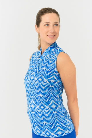 The close up side view of the Pure Golf Rise Santorini Skies Sleeveless Ladies' Golf Polo Shirt highlights a stunning Ikat-inspired design in shades of blue and white. With a regular fit and 4-way stretch, it ensures comfort and a flattering silhouette for all body types. The mandarin collar adds an elegant touch. Crafted from 95% polyester and 5% spandex, the polo offers anti-crease, anti-static, and quick-dry properties, along with UPF 50+ sun protection. It is paired with our Royal Blue Skort.