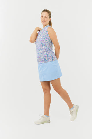 The model is wearing the Pure Golf Rise Over Eighteen Sleeveless Ladies' Golf Polo Shirt, featuring the "Over Eighteen" print with subtle cocktail motifs in soft hues of blue, lilac, and pink. The shirt is designed with a mid zip and white trim, providing a regular fit and 4-way stretch for comfort on all body types. A mandarin collar adds a touch of sophistication. Crafted from 95% polyester and 5% spandex, it offers anti-crease, anti-static, and quick-dry benefits, as well as UPF 50+ sun protection.