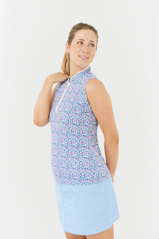 The model shot from the side highlights the Pure Golf Rise Over Eighteen Sleeveless Ladies' Golf Polo Shirt, featuring the “Over Eighteen” print with subtle cocktail motifs in a soft blend of blues, lilacs, and pinks. It includes a mid zip with white trim, offering a regular fit and 4-way stretch for comfort across all body types. The mandarin collar adds an elegant touch. Made from 95% polyester and 5% spandex, designed with anti-crease, anti-static, and quick-dry properties, plus UPF 50+ sun protection.