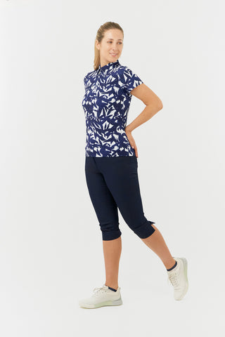 The Pure Golf Amity full-length side model shot highlights the short-sleeve ladies' golf polo shirt, featuring a botanical print in navy and white, paired with our Trust Capri's in navy. This regular-fit polo shirt offers a 4-way stretch for both comfort and a flattering fit on all body types. Its traditional collar adds a classic and stylish touch. The shirt is designed to be anti-crease, anti-static, and quick-drying, with UPF 50+ protection. Made from 95% polyester and 5% spandex