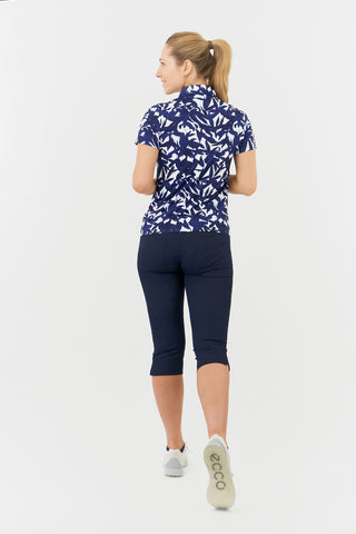 The Pure Golf Amity full-length model shot features the back of the short-sleeve ladies' golf polo shirt, adorned with a botanical print in navy and white. This regular-fit polo shirt provides a 4-way stretch for comfort and a flattering fit on all body types. Its traditional collar adds a classic and stylish touch. Designed to be anti-crease, anti-static, and quick-drying, the shirt also offers UPF 50+ protection. Made from 95% polyester and 5% spandex. Paired with our Navy Trust Capri to complete the look