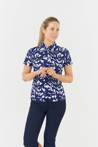 The Pure Golf Amity part full-length model shot presents the short-sleeve ladies' golf polo shirt, featuring a botanical print in navy and white, paired with navy Trust Capri's. This regular-fit polo shirt offers a 4-way stretch for both comfort and a flattering fit for all body types. Its traditional collar adds a classic and stylish touch. The shirt is crafted to be anti-crease, anti-static, and quick-drying, with UPF 50+ protection. Made from 95% polyester and 5% spandex