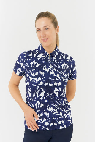 The Pure Golf Amity model shot showcases the short sleeve ladies' golf polo shirt, featuring a botanical print in Navy and white. This regular-fit polo shirt offers a 4-way stretch for comfort and a flattering fit on all body types. With its traditional collar, it delivers a classic and stylish look. The shirt is designed to be anti-crease, anti-static, and quick-drying, with UPF 50+ protection. Made from 95% Polyester and 5% Spandex, it ensures both performance and style.