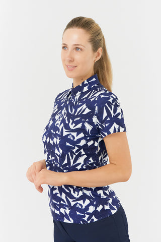 The Pure Golf Amity top-half, side model shot showcases the short-sleeve ladies' golf polo shirt, featuring a botanical print in navy and white. This regular-fit polo shirt offers a 4-way stretch for both comfort and a flattering fit on all body types. Its traditional collar adds a classic and stylish touch. The shirt is designed to be anti-crease, anti-static, and quick-drying, with UPF 50+ protection. Made from 95% polyester and 5% spandex.