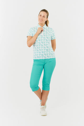 Full model shot of the Pure Golf Amity Short Sleeve Ladies' Golf Polo Shirt in Floating Palms White, features a striking botanical print in Ocean against a crisp white background. This regular-fit polo offers a 4-way stretch for comfort and a flattering fit on all body types. The traditional collar adds a classic touch. Designed to be anti-crease, anti-static, and quick-drying, the shirt also offers UPF 50+ sun protection, made from 95% Polyester and 5% Spandex. Paired with our Ocean Trust Capri. 