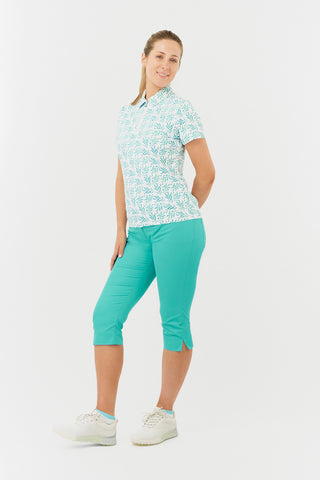 The side view model shot of the Pure Golf Amity Short Sleeve Ladies' Golf Polo Shirt in Floating Palms White showcases a striking botanical print in Ocean against a crisp white background. This regular-fit polo offers a 4-way stretch for comfort and a flattering fit on all body types. The traditional collar adds a classic touch. Designed to be anti-crease, anti-static, and quick-drying, the shirt also provides UPF 50+ sun protection, crafted from 95% Polyester and 5% Spandex.