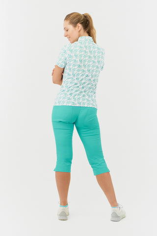 The full length model shot displays the back view of the Pure Golf Amity Short Sleeve Ladies' Golf Polo Shirt in Floating Palms White, featuring a striking botanical print in Ocean on a crisp white background. This regular-fit polo offers a 4-way stretch for comfort and a flattering fit for all body types. The traditional collar adds a classic touch. Designed to be anti-crease, anti-static, and quick-drying, the shirt also provides UPF 50+ sun protection, crafted from 95% Polyester and 5% Spandex.