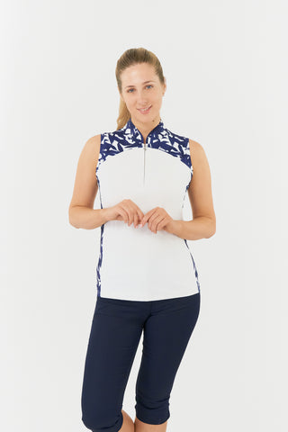 The front shot of the Pure Golf Freda model highlights the sleeveless ladies' golf polo shirt, featuring a botanical print in navy and white across the shoulder, sides, and mandarin collar, with a white body. This regular-fit polo shirt offers a 4-way stretch for comfort and a flattering fit on all body types. Designed to be anti-crease, anti-static, and quick-drying, the shirt also provides UPF 50+ protection. Made from 95% Polyester and 5% Spandex. Paired with Navy Trust Capri's.