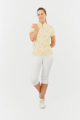 The Pure Golf Ellen short-sleeve ladies' polo shirt model shot features a front view showcasing the sunkissed print and honey hues. Paired with white Bermuda Shorts. Designed with a regular fit, it offers a 4-way stretch for comfort and a flattering shape on all body types. The stylish sweetheart collar adds a fashionable touch. This polo is made from 95% Polyester and 5% Spandex, offering anti-crease, anti-static, and quick-dry properties, along with UPF 50+ sun protection.