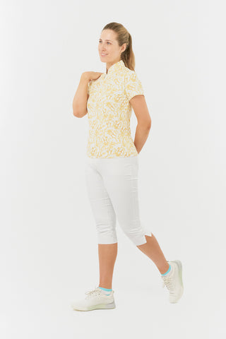 The Pure Golf Ellen short-sleeve ladies' polo shirt is shown in a slight side view, highlighting the sunkissed print and warm honey tones. It is paired with white Bermuda shorts. Designed for a regular fit, the polo provides a 4-way stretch for comfort and a flattering silhouette on all body types. The chic sweetheart collar adds a stylish flair. Made from 95% polyester and 5% spandex, the polo offers anti-crease, anti-static, and quick-dry benefits, along with UPF 50+ sun protection..