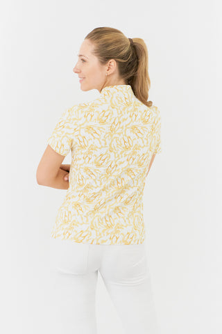 The Pure Golf Ellen short-sleeve ladies' polo shirt is featured in a back view, highlighting the sunkissed print and warm honey tones. It is paired with white Bermuda shorts. Designed with a regular fit, the polo offers a 4-way stretch for comfort and a flattering silhouette on all body types. The chic sweetheart collar adds a stylish touch. Made from 95% polyester and 5% spandex, the polo provides anti-crease, anti-static, and quick-dry benefits, along with UPF 50+ sun protection.