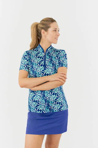 The Pure Golf Ellen short-sleeve ladies' polo shirt model shot features a front view showcasing prints with a summery aquatic essence of multi-blue tones. Paired with Yale Navy Skort. Designed with a regular fit, it offers a 4-way stretch for comfort and a flattering shape on all body types. The stylish sweetheart collar adds a fashionable touch. This polo is made from 95% Polyester and 5% Spandex, offering anti-crease, anti-static, and quick-dry properties, along with UPF 50+ sun protection.