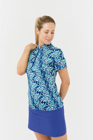 The Pure Golf Ellen short-sleeve ladies' polo shirt model shot features a slight side view showcasing prints with a summery aquatic essence of multi-blue tones. Paired with Yale Navy Skort. Designed with a regular fit, it offers a 4-way stretch for comfort and a flattering shape on all body types. The stylish sweetheart collar adds a fashionable touch. This polo is made from 95% Polyester and 5% Spandex, offering anti-crease, anti-static, and quick-dry properties, along with UPF 50+ sun protection.