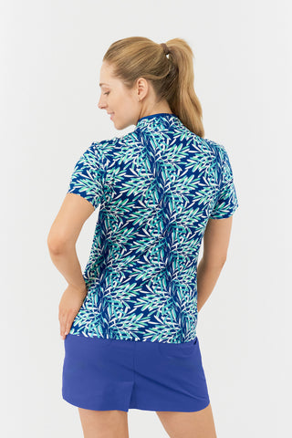 The Pure Golf Ellen short-sleeve ladies' polo shirt, featured in a model shot from the back, showcases prints with a summery aquatic vibe in multi-blue tones. It is paired with a Yale Navy Skort for a polished look. Designed with a regular fit, the polo offers a 4-way stretch for comfort and a flattering shape on all body types. The chic sweetheart collar adds a fashionable touch. Made from 95% Polyester and 5% Spandex, this polo is anti-crease, anti-static, and quick-drying, while providing UPF 50+