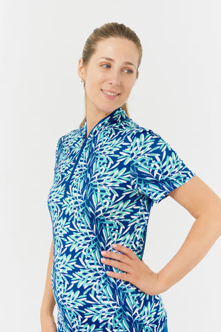 The Pure Golf Ellen short-sleeve ladies' polo shirt, featured in a model shot from the side showcases prints with a summery aquatic vibe in multi-blue tones. Designed with a regular fit, the polo offers a 4-way stretch for comfort and a flattering shape on all body types. The chic sweetheart collar adds a fashionable touch. Made from 95% Polyester and 5% Spandex, this polo is anti-crease, anti-static, and quick-drying, while providing UPF 50+ 