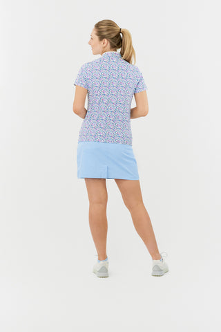 The Pure Golf Ellen short-sleeve ladies' polo shirt model shot full length back view showcasing our Over Eighteen Print featuring cocktail motifs in a subtle scale. Designed with a regular fit, it offers a 4-way stretch for comfort and a flattering shape on all body types. The stylish sweetheart collar adds a fashionable touch. This polo is made from 95% Polyester and 5% Spandex, offering anti-crease, anti-static, and quick-dry properties, along with UPF 50+ sun protection. Paired with a light blue skort. 