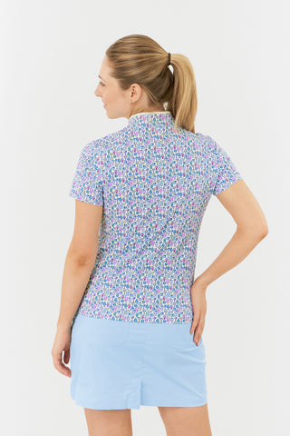 The Pure Golf Ellen short-sleeve ladies' polo shirt model shot back view showcasing our Over Eighteen Print featuring cocktail motifs in a subtle scale. Designed with a regular fit, it offers a 4-way stretch for comfort and a flattering shape on all body types. The stylish sweetheart collar adds a fashionable touch. This polo is made from 95% Polyester and 5% Spandex, offering anti-crease, anti-static, and quick-dry properties, along with UPF 50+ sun protection. Paired with a light blue skort. 