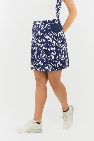 The Pure Golf lifestyle shot of the Accuracy Skort with Side Zip in Wild Peony Navy features a stunning botanical print in navy and white. Made from 4-way stretch material, this skort offers unrestricted movement, while the detachable shorts provide added coverage. The convenient side zipper closure ensures easy wear, and the stylish back panel adds a flattering detail. Designed with anti-crease, anti-static, and quick-drying properties, it also provides UPF 50+ protection. Crafted from 100% Polyester. 