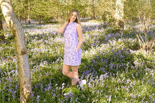 The Pure Golf lifestyle image highlighting the Heather Sleeveless Dress features an elegant two-tone blend of purple and lilac, with a slimming lilac side panel. Made from 4-way stretch fabric, it ensures maximum flexibility, while removable shorts provide added coverage. The mock neck collar adds a contemporary, flattering detail for all body shapes. This dress is designed to be anti-crease, anti-static, and quick-drying, while offering UPF 50+ protection. It is crafted from 95% polyester and 5% spandex.