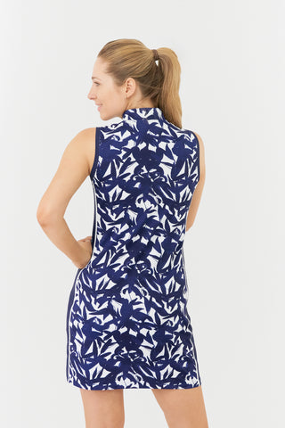 The Pure Golf model shot shows the back of the Heather Sleeveless dress. The dress has a botanical print in navy and white, accented by a flattering navy side panel. Crafted from 4-way stretch material for maximum flexibility and unrestricted movement, it also features detachable shorts for added versatility and coverage. The mock neck collar provides a sleek, modern look while ensuring a flattering fit for all body types. Designed to be anti-crease, anti-static, and quick-drying, it also offers UPF 50+