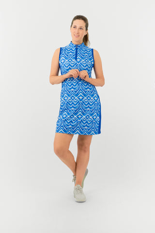 The Pure Golf model shot of the Sophie Sleeveless dress features the Santorini Skies print in shades of blue and white, complemented by a Royal Blue side panel. Crafted from 4-way stretch fabric, it offers flexibility and freedom of movement, with detachable shorts for added coverage. The mock neck collar provides a sleek, modern look, and the dress offers a flattering fit for all body types. Designed to resist creasing, static, and moisture, it also provides UPF 50+ protection.  