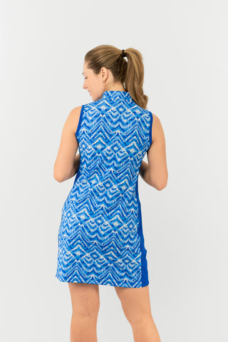 The Pure Golf model shot shows the back of the Sophie Sleeveless dress features the Santorini Skies print in shades of blue and white, complemented by a Royal Blue side panel for a flattering touch. Crafted from 4-way stretch fabric, it offers freedom of movement, with detachable shorts for added coverage. The mock neck collar provides a sleek, modern look, and the dress offers a flattering fit for all body types. Designed to resist creasing, static, and moisture, it also provides UPF 50+ protection. 