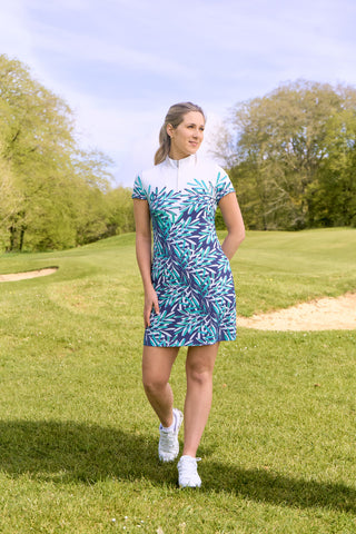 The Pure Golf lifestyle shot of the Carly Cap Sleeve dress features a summary aquatic of multi-blue and ocean tones with a print of floating palms from the chest downwards. Longer length dress made in 4-way stretch material for maximum flexibility with detachable shorts for coverage. Flattering fit on all body types. The mock neck collar offers a sleek, modern look. Designed to be anti-crease, anti-static, and quick drying, it also provides UPF 50+ protection. Made from 95% Polyester and 5% Spandex.