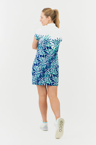 The Pure Golf model shot showing the back of the Carly Cap Sleeve dress showcases an aquatic design in shades of blue and ocean hues, featuring a print of floating palms from the chest down. This longer-length dress is crafted from 4-way stretch fabric for enhanced flexibility, with detachable shorts for added coverage. Its flattering fit suits all body types, while the mock neck collar delivers a sleek style. Designed to resist creasing, static, and moisture, the dress also offers UPF 50+ protection. 