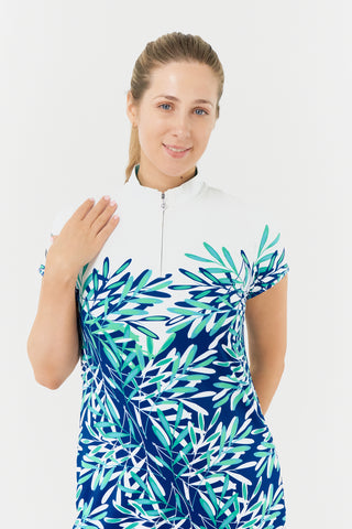 The close-up model shot of the Pure Golf Carly Cap Sleeve dress in an aquatic design of various shades of blue and ocean tones, accented with a floating palm print from the chest down. This longer-length dress is made from 4-way stretch fabric for optimal flexibility and includes detachable shorts for extra coverage. Its flattering fit complements all body types, and the mock neck collar adds a sleek, modern touch. Designed to resist creasing, static, and moisture, the dress also provides UPF 50+ protection