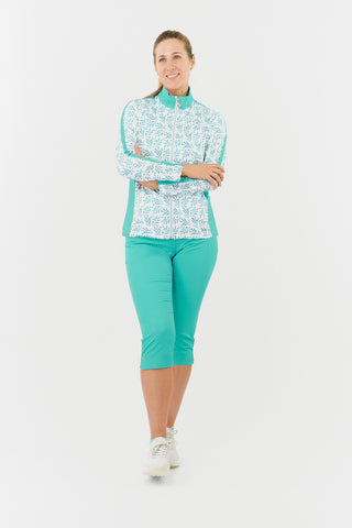 The model shot of the Pure Golf Gella Ladies Golf Mid Layer Jacket in Floating Palms White. A striking all-over botanical print on a crisp white background with Ocean block colour on the mock neck, sides and a thin stripe down each arm. This regular-fit polo offers a 4-way stretch for a flattering fit on all body types. Designed to be anti-crease, anti-static, and quick-drying, the shirt also offers UPF 50+ sun protection, made from 95% Polyester and 5% Spandex. 