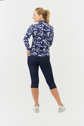 The Pure Golf Serenity long-sleeve ladies' golf zip top model shot showcasing a back view of our botanical print in Wild Peony Navy. Designed with a regular fit, it offers a 4-way stretch for comfort and a flattering shape on all body types. The mock neck collar offers a sleek, modern look and extra coverage. Made from 95% Polyester and 5% Spandex, offering anti-crease, anti-static, and quick-dry properties, along with UPF 50+ sun protection. Paired with Navy Trust Capri's.  