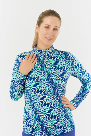 The Pure Golf model shot of the Serenity long-sleeve ladies' golf zip top showcases a soothing aquatic design in multi-blue and ocean tones, featuring a floating palms print. Designed with a regular fit, it offers 4-way stretch for comfort and a flattering shape on all body types. The mock neck collar adds a sleek, touch. Made from 95% Polyester and 5% Spandex, with anti-crease, anti-static, and quick-dry properties, along with UPF 50+ sun protection.