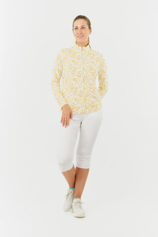 A model shot of the Pure Golf Balance Sun Kissed Long Sleeve Ladies' Golf Zip Top from our Ray Flower collection features a beautiful print in warm honey hues. With a regular fit and 4-way stretch, it ensures comfort for all body types. The mock neck collar adds a sleek look, while mesh white sleeve panels enhance breathability. Crafted from 95% polyester and 5% spandex, it offers anti-crease, anti-static, and quick-dry properties, along with UPF 50+ protection. Paired with White Trust Capri's.