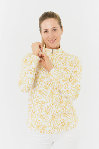 A close-up model shot of the Pure Golf Balance Sun Kissed Long Sleeve Ladies' Golf Zip Top from our Ray Flower collection shows a beautiful print in warm honey hues. With a regular fit and 4-way stretch, it ensures comfort for all body types. The mock neck collar adds a sleek touch, while white mesh sleeve panels enhance breathability. Crafted from 95% polyester and 5% spandex, it offers anti-crease, anti-static, and quick-dry properties, along with UPF 50+ protection. Looks stylish with White Trust Capri's