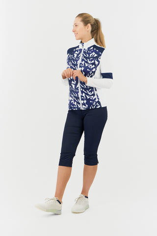 The Pure Golf Galena model showcases the mid-layer jacket in Wild Peony, featuring a botanical navy and white print on the body and inner neck, with white sleeves, a navy band around the elbow, and a navy block across the shoulders. Designed for comfort and a flattering fit, it offers 4-way stretch to suit all body types. The jacket is anti-crease, anti-static, and quick-drying, and provides UPF 50+ sun protection. It is made from 95% Polyester and 5% Spandex.