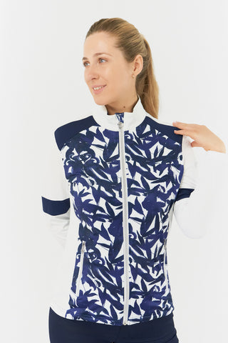 The Pure Golf Galena model shot highlights the front of the mid-layer jacket in Wild Peony, featuring a botanical navy and white print on the body and inner neck, white sleeves, a navy band around the elbow, and a navy block across the shoulders. Designed for comfort and a flattering fit, the jacket offers 4-way stretch to suit all body types. It is anti-crease, anti-static, quick-drying, and provides UPF 50+ sun protection. Made from 95% Polyester and 5% Spandex.