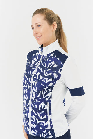 The Pure Golf Galena model shot showcases the side view of the mid-layer jacket in Wild Peony, featuring a botanical navy and white print on the body and inner neck, white sleeves, a navy band around the elbow, and a navy block across the shoulders. Designed for comfort and a flattering fit, the jacket offers 4-way stretch to suit all body types. It is anti-crease, anti-static, quick-drying, and provides UPF 50+ sun protection. Made from 95% Polyester and 5% Spandex.