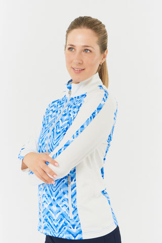 The close-up side model shot of the Pure Golf Gia Mid Layer Jacket in Santorini Skies highlights its striking Ikat-inspired blue print, beautifully placed inside the mock collar, across the main body, with a slim seam running from the shoulders down the sleeves. The 4-way stretch ensures a flattering fit for all body types, while its anti-crease, anti-static, and quick-drying properties, along with UPF 50+ sun protection, make it both practical and stylish. Made from 95% Polyester and 5% Spandex. 